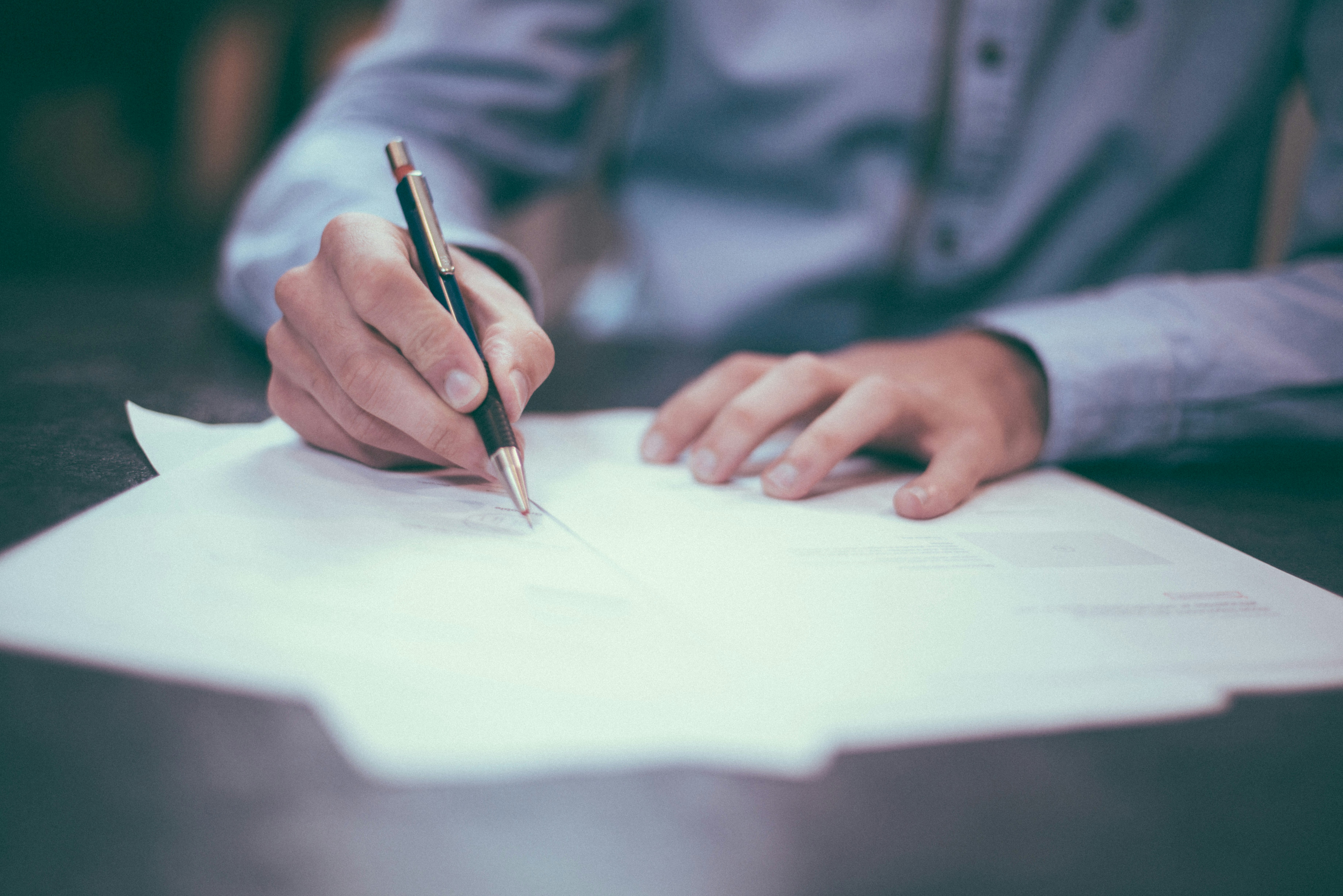 A photo of a white person writing on a few pieces of paper, on a dark table.