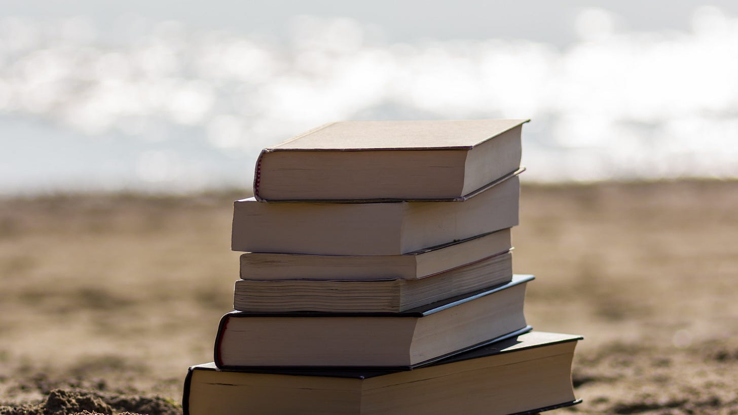 Stack of books on sand. The ocean glimmers in the background